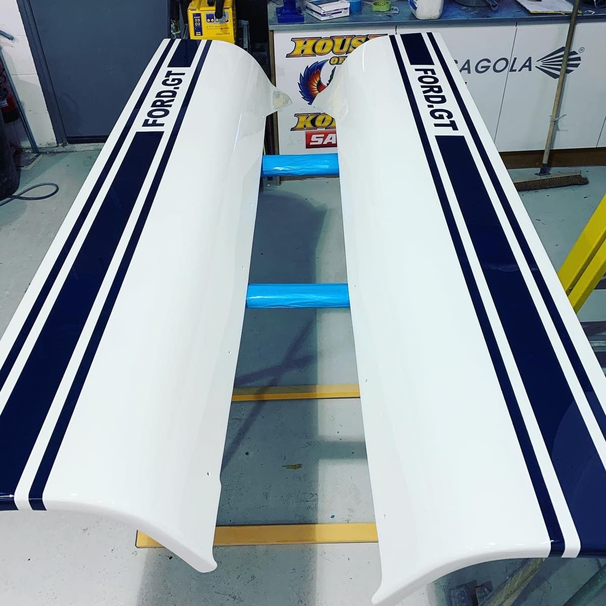 Two white Ford GT sill panels with navy stripes, laid out on trestles after painting